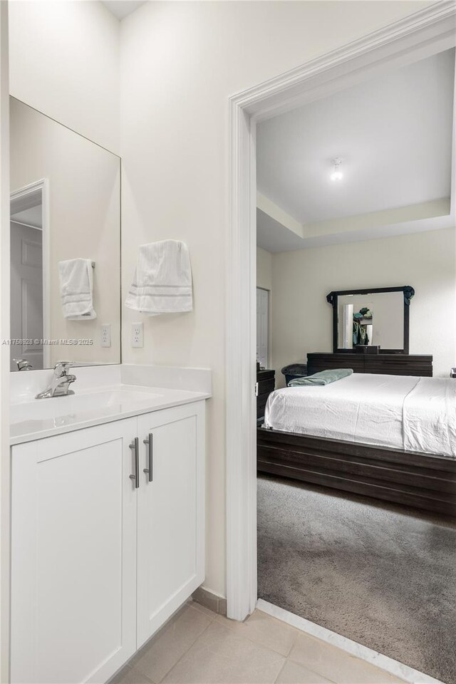 bedroom with a tray ceiling, a sink, and light tile patterned floors