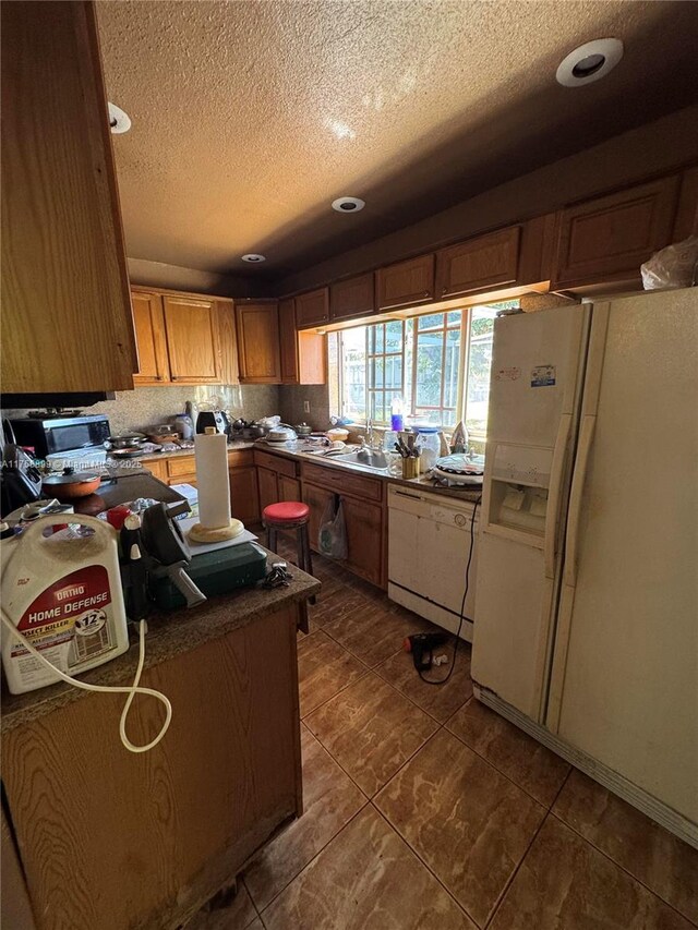 kitchen featuring dark countertops, decorative backsplash, a sink, a textured ceiling, and white fridge with ice dispenser