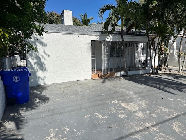 exterior space with roof with shingles, a chimney, and stucco siding