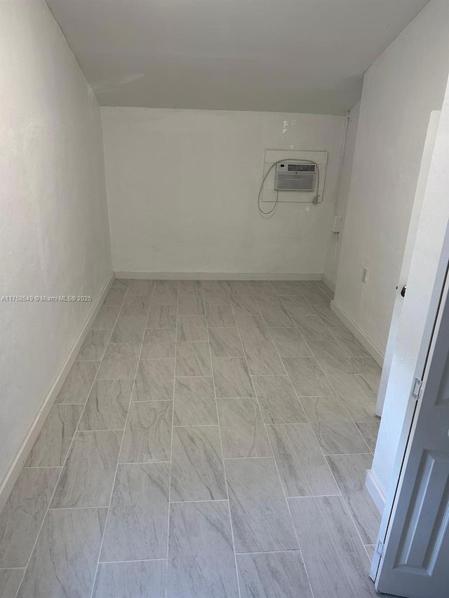 empty room featuring a wall mounted air conditioner and baseboards