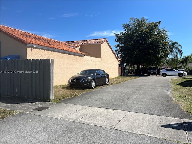 view of side of property with a tile roof, fence, and stucco siding