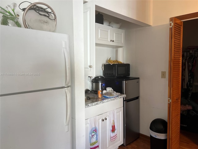 kitchen featuring black microwave, white cabinets, light countertops, and freestanding refrigerator