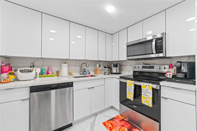 kitchen with modern cabinets, appliances with stainless steel finishes, marble finish floor, white cabinetry, and a sink