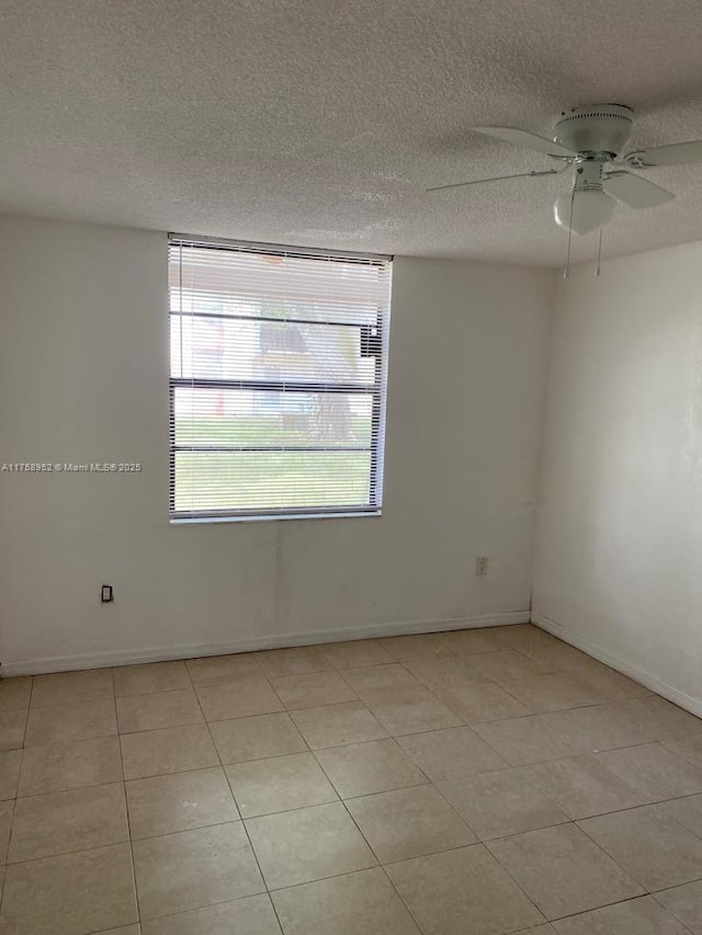 empty room featuring light tile patterned flooring, ceiling fan, a textured ceiling, and baseboards