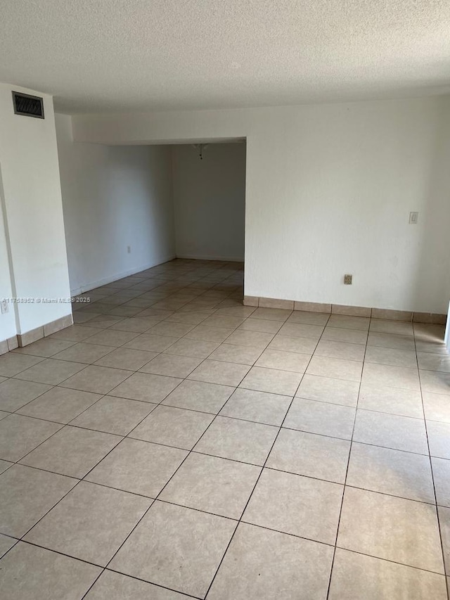 spare room featuring visible vents, a textured ceiling, baseboards, and light tile patterned floors