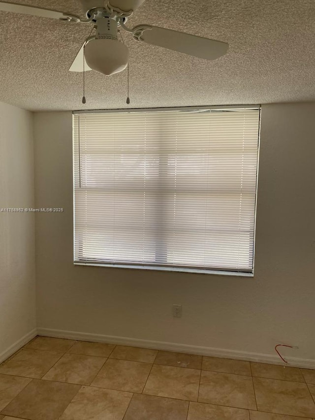 empty room with light tile patterned flooring, ceiling fan, a textured ceiling, and baseboards