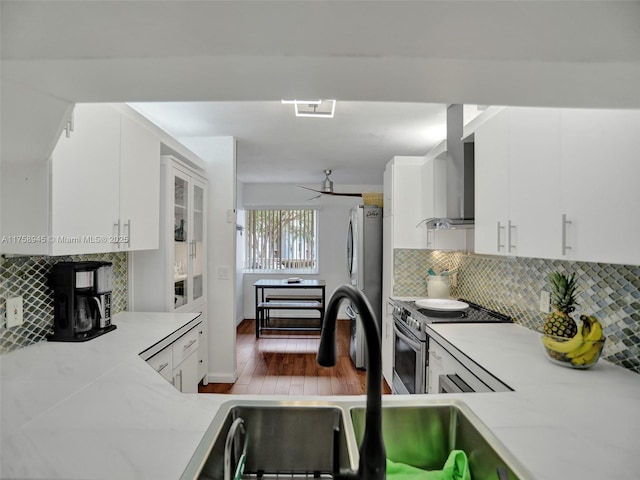 kitchen featuring appliances with stainless steel finishes, wall chimney exhaust hood, white cabinets, and light countertops