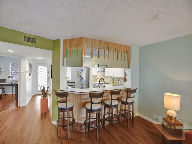 kitchen featuring wood finished floors, visible vents, freestanding refrigerator, a kitchen breakfast bar, and backsplash