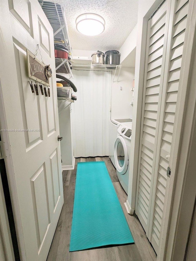 washroom featuring washer and clothes dryer, laundry area, a textured ceiling, and wood finished floors