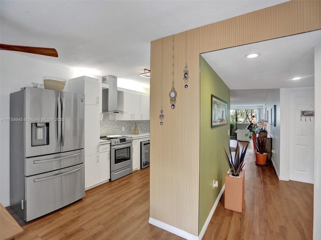 kitchen with beverage cooler, light wood-style flooring, white cabinets, appliances with stainless steel finishes, and wall chimney range hood