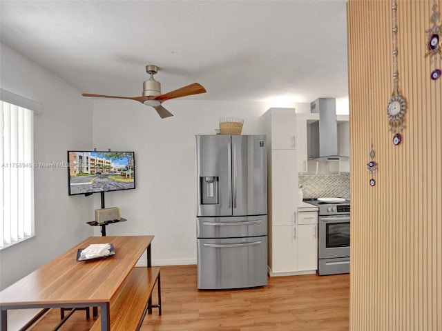 kitchen featuring light wood-style flooring, backsplash, appliances with stainless steel finishes, white cabinets, and wall chimney range hood