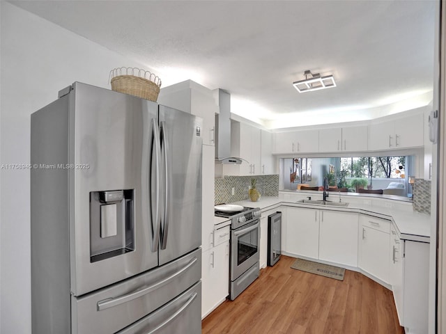 kitchen featuring a sink, light countertops, light wood-style floors, appliances with stainless steel finishes, and wall chimney range hood