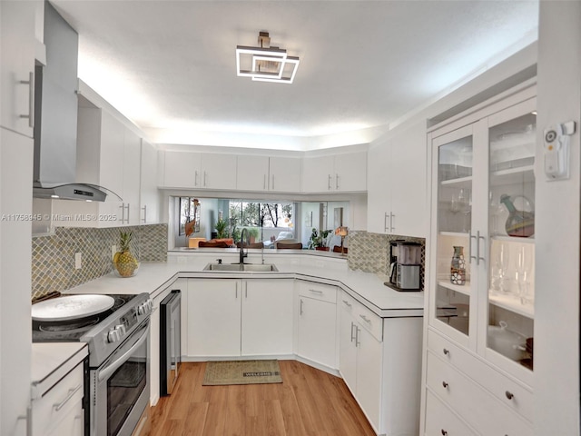 kitchen with a sink, stainless steel electric range, wall chimney exhaust hood, and light countertops