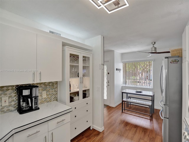 kitchen with backsplash, wood finished floors, white cabinetry, freestanding refrigerator, and light countertops