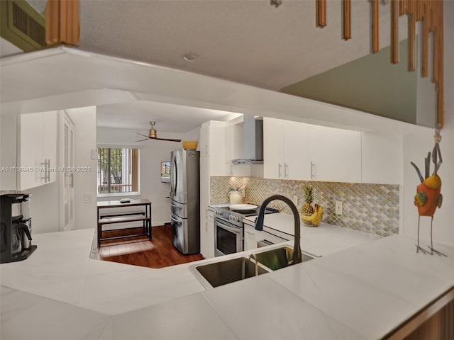 kitchen with tasteful backsplash, wall chimney range hood, light countertops, stainless steel appliances, and a sink