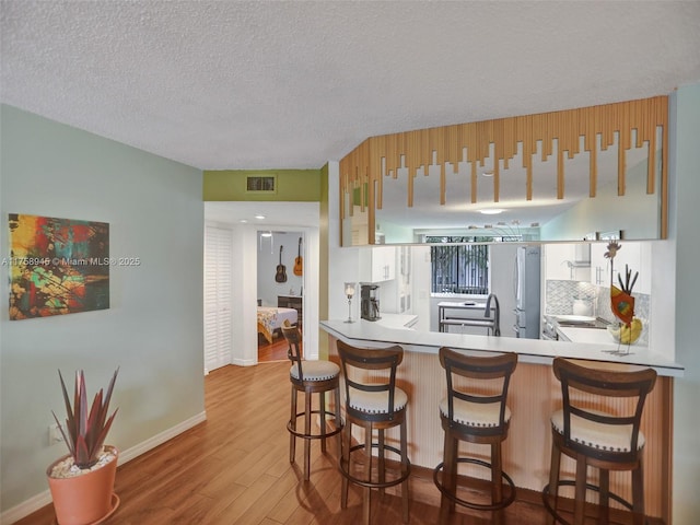 kitchen featuring visible vents, a textured ceiling, wood finished floors, freestanding refrigerator, and decorative backsplash