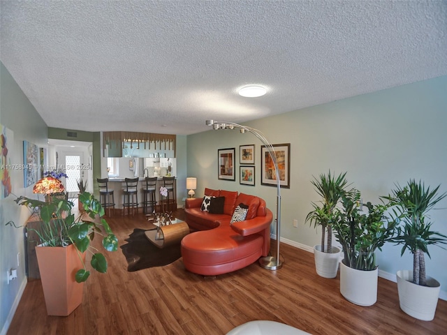 living area featuring visible vents, a textured ceiling, baseboards, and wood finished floors