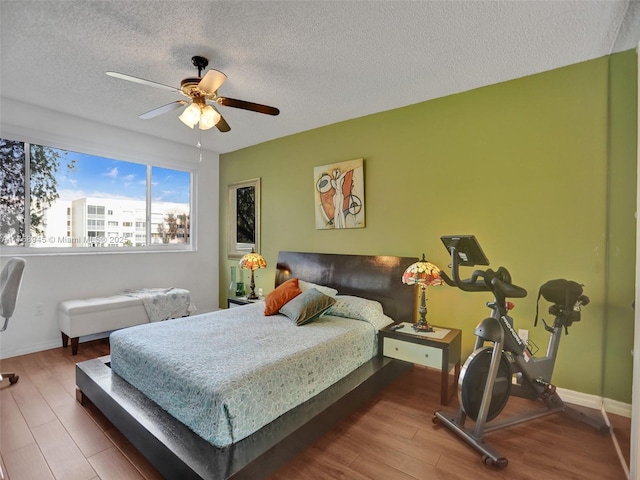 bedroom featuring a ceiling fan, wood finished floors, baseboards, and a textured ceiling