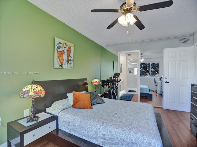 bedroom with ceiling fan, visible vents, a textured ceiling, and wood finished floors