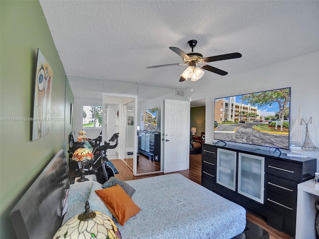 bedroom featuring ceiling fan, visible vents, a textured ceiling, and dark wood-style floors