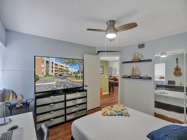 bedroom with visible vents, a textured ceiling, a ceiling fan, and wood finished floors