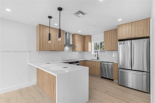 kitchen with stainless steel appliances, a peninsula, a sink, visible vents, and wall chimney range hood