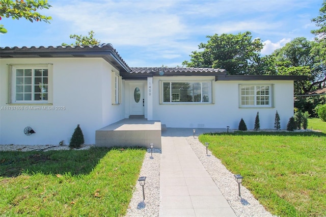 ranch-style home with a front yard, a tile roof, and stucco siding