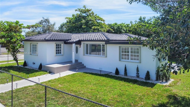 view of front of house featuring a tiled roof, a front yard, fence, and stucco siding