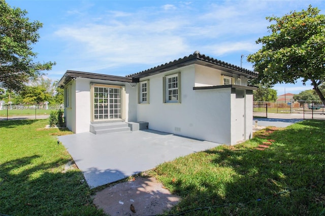 rear view of property featuring entry steps, a lawn, a patio, fence, and stucco siding