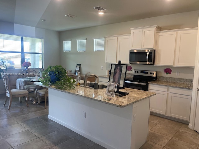 kitchen with an island with sink, a sink, light stone counters, white cabinetry, and appliances with stainless steel finishes