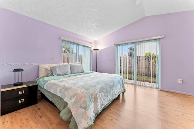 bedroom with vaulted ceiling, light wood-style floors, multiple windows, and access to exterior