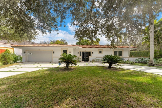 mediterranean / spanish-style house with stucco siding, driveway, a tile roof, a front yard, and a garage