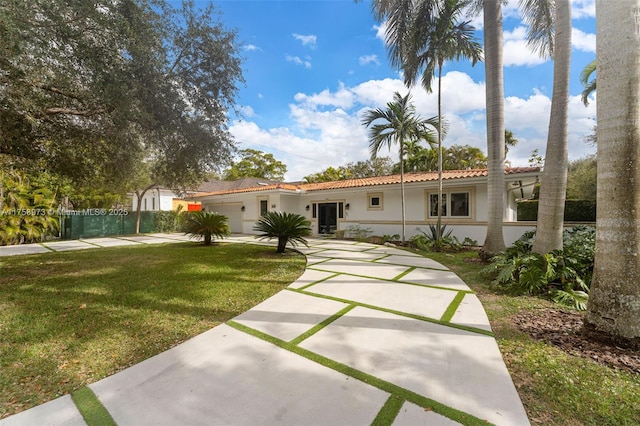 view of front facade with a tile roof, a front yard, stucco siding, a garage, and driveway