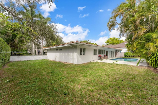 back of house featuring a patio area, a lawn, an outdoor pool, and stucco siding