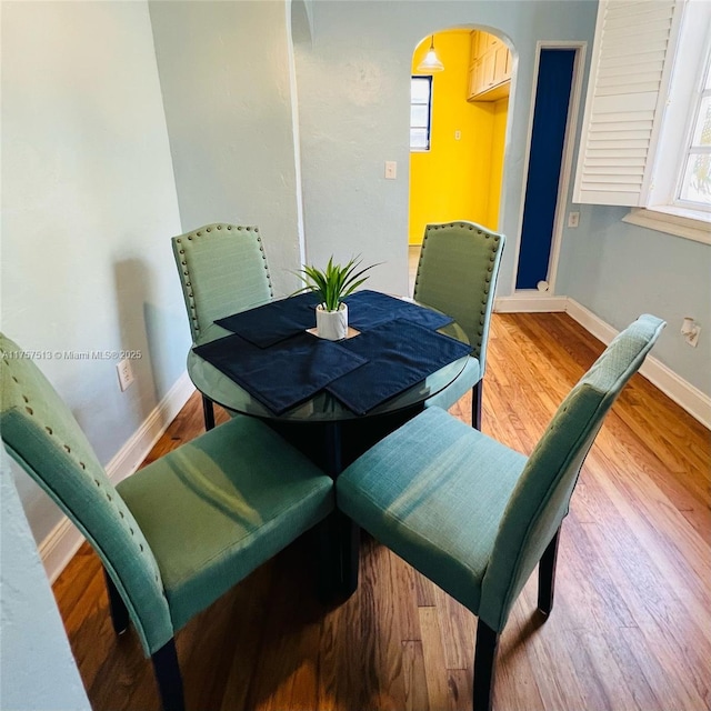 dining space with arched walkways, wood finished floors, and baseboards