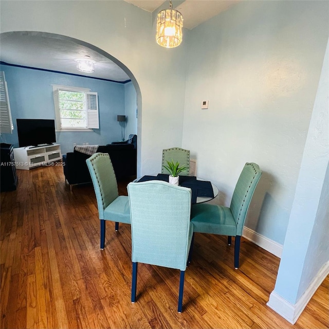 dining area featuring arched walkways, baseboards, and wood finished floors