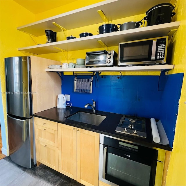 kitchen featuring open shelves, stainless steel appliances, dark countertops, light brown cabinets, and a sink