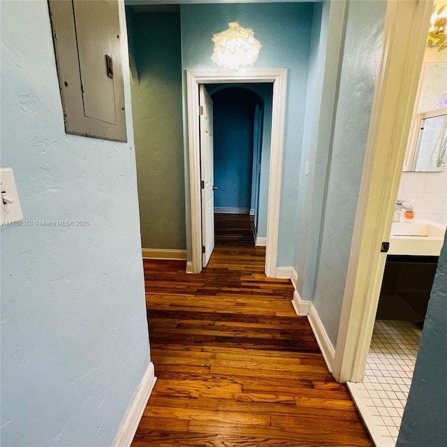 corridor featuring electric panel, baseboards, wood finished floors, and a textured wall