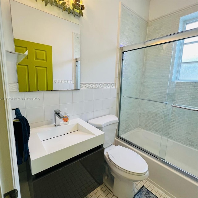 full bathroom with toilet, tile patterned flooring, combined bath / shower with glass door, vanity, and tile walls