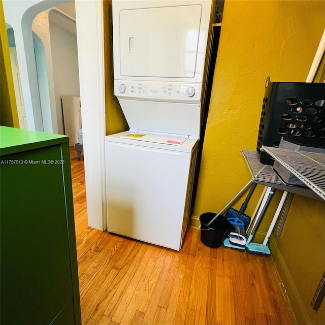 washroom featuring arched walkways, laundry area, light wood-type flooring, and stacked washer / drying machine