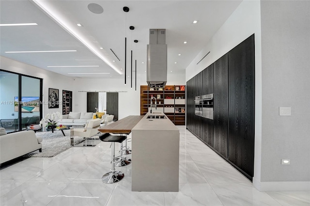 kitchen with a breakfast bar area, a kitchen island with sink, recessed lighting, dark cabinets, and modern cabinets