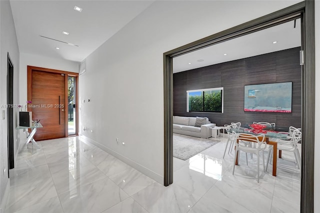 corridor featuring marble finish floor, an accent wall, and baseboards