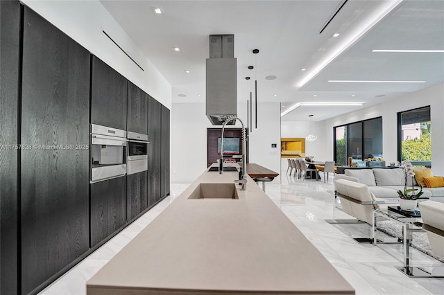 kitchen with oven, dark cabinets, open floor plan, marble finish floor, and light countertops