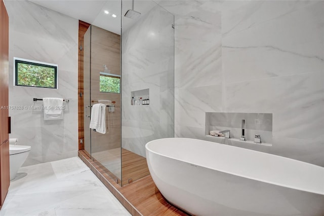 full bathroom featuring toilet, a soaking tub, a shower stall, and tile walls