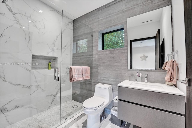 bathroom featuring toilet, vanity, a marble finish shower, and tile walls