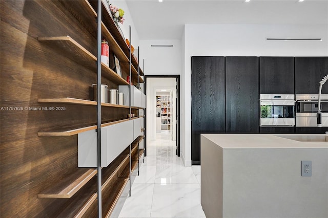 interior space featuring dark cabinets, stainless steel double oven, and marble finish floor