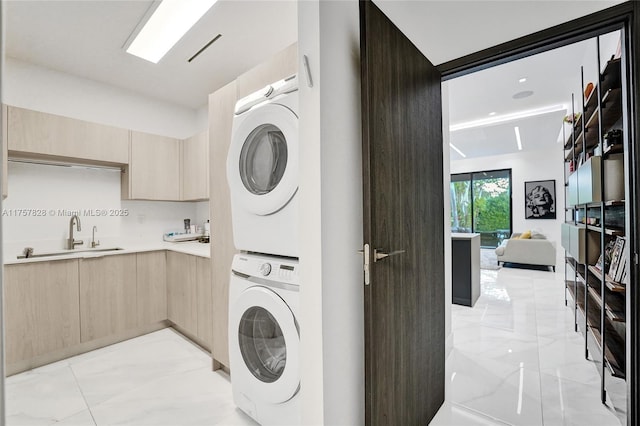 clothes washing area with marble finish floor, stacked washing maching and dryer, a sink, and laundry area