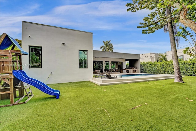 back of house featuring a yard, a playground, a fenced in pool, and stucco siding