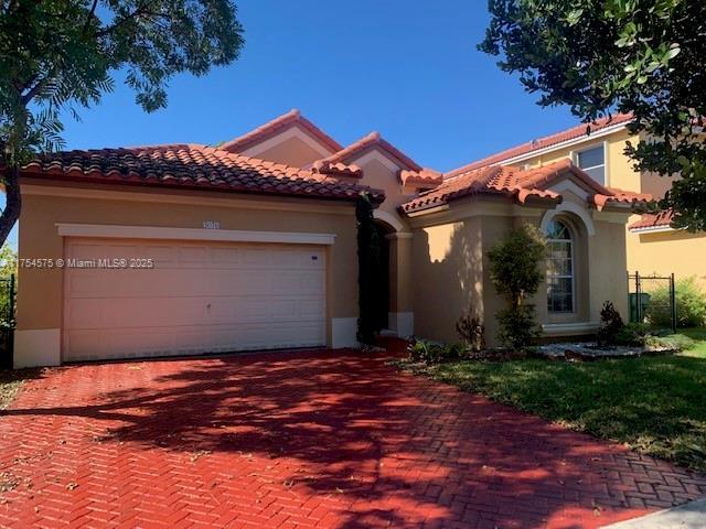 mediterranean / spanish house with stucco siding, decorative driveway, an attached garage, and a tiled roof