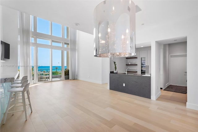 unfurnished living room with a towering ceiling, light wood-style floors, baseboards, and a sink